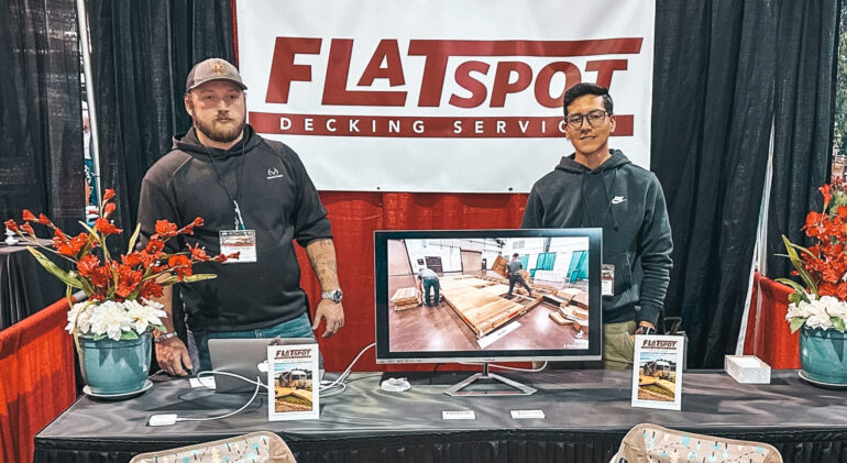 The photo shows two men in front of the Flatspot Decking Services stand at a trade fair for wooden decking and glamping.
