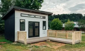 A small wooden house with a wooden deck and wooden railing in front of it.