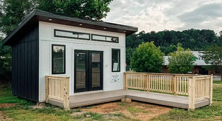 A small wooden house with a wooden deck and wooden railing in front of it.