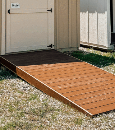 A small shed with a beige exterior featuring a brown composite deck ramp made of Trex boards, providing easy access to the entrance.