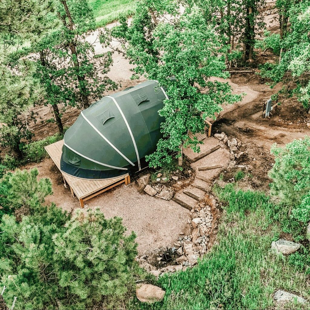 Glamping tent on a wooden deck with wooden railing in the forest.