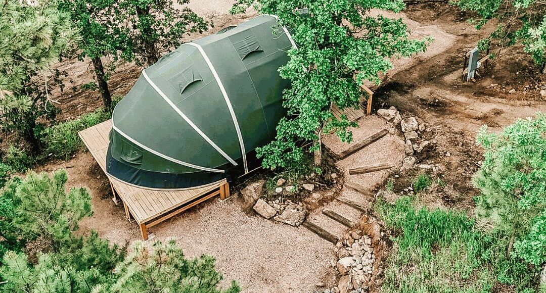 Glamping tent on a wooden deck with wooden railing in the forest.