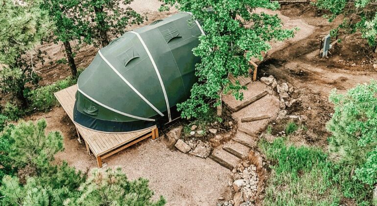 Glamping tent on a wooden deck with wooden railing in the forest.