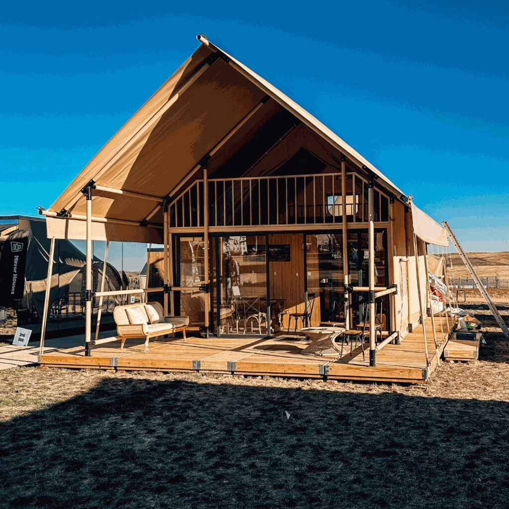 A gabled glamping tent with a wooden mezzanine standing on a wooden deck by Flatspot Decking Services during the Glamping Show Americas.