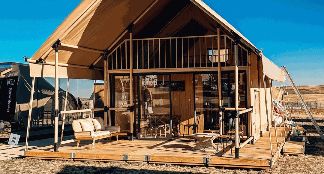 A gabled glamping tent with a wooden mezzanine standing on a wooden deck by Flatspot Decking Services during the Glamping Show Americas.