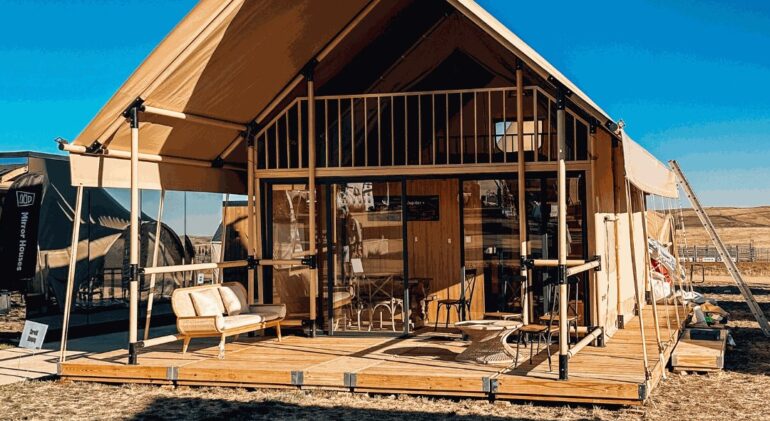 A gabled glamping tent with a wooden mezzanine standing on a wooden deck by Flatspot Decking Services during the Glamping Show Americas.
