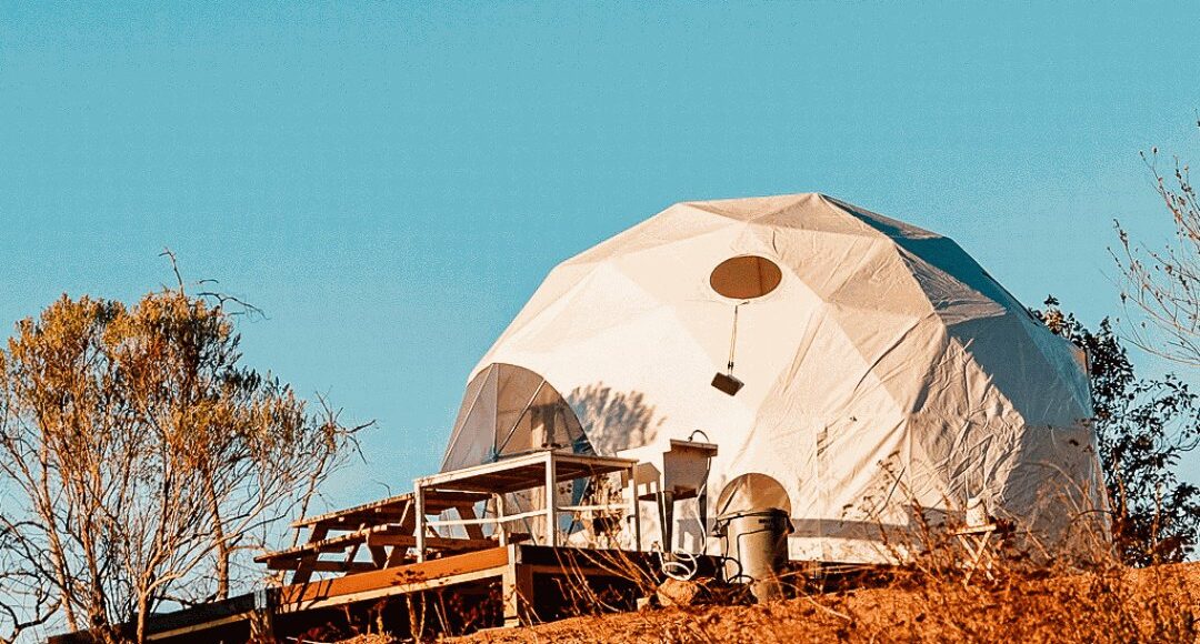 A white geodesic tent on a wooden deck.
