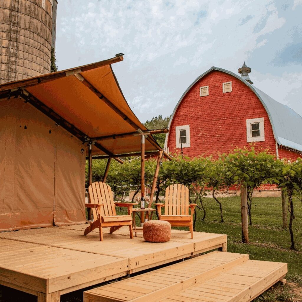 A wooden deck with a table, chairs, a pouf, and a gable tent. The tent is located near the wine cellar.